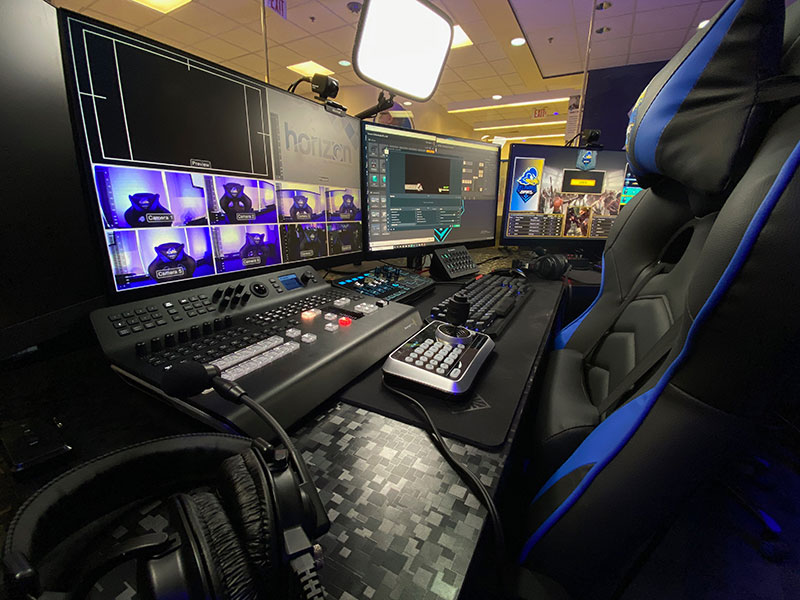 Table with 3 large monitors, multiple keyboards, headset and other equipment.