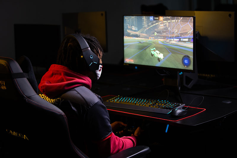 Person sitting in a chair looking intently at a monitor. Person is wearing headphones and using a game controller.