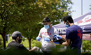 3 people outside wearing masks and gloves, distributing equipment