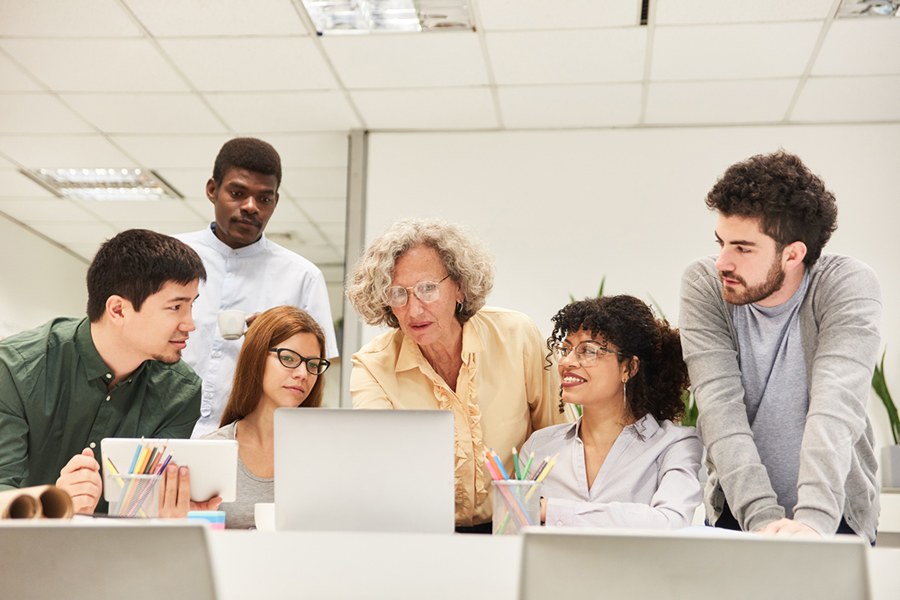 faculty member looking at laptop with group of students