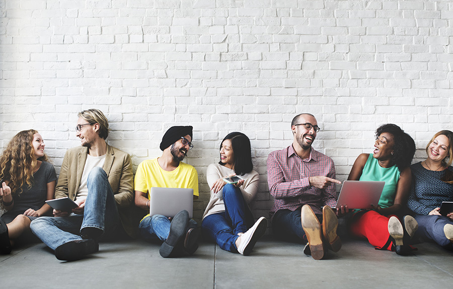 students siting against a white brick wall and talking