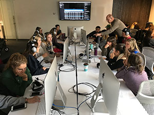 Group of students around a table with computer monitors.