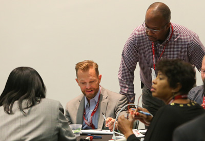 3 people sitting in a group with a presenter standing talking to them.