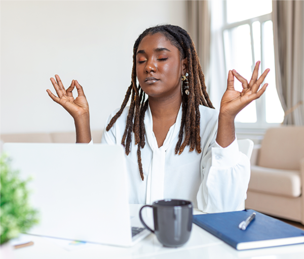 A person sitting in front of a laptop with eyes closed and meditating.